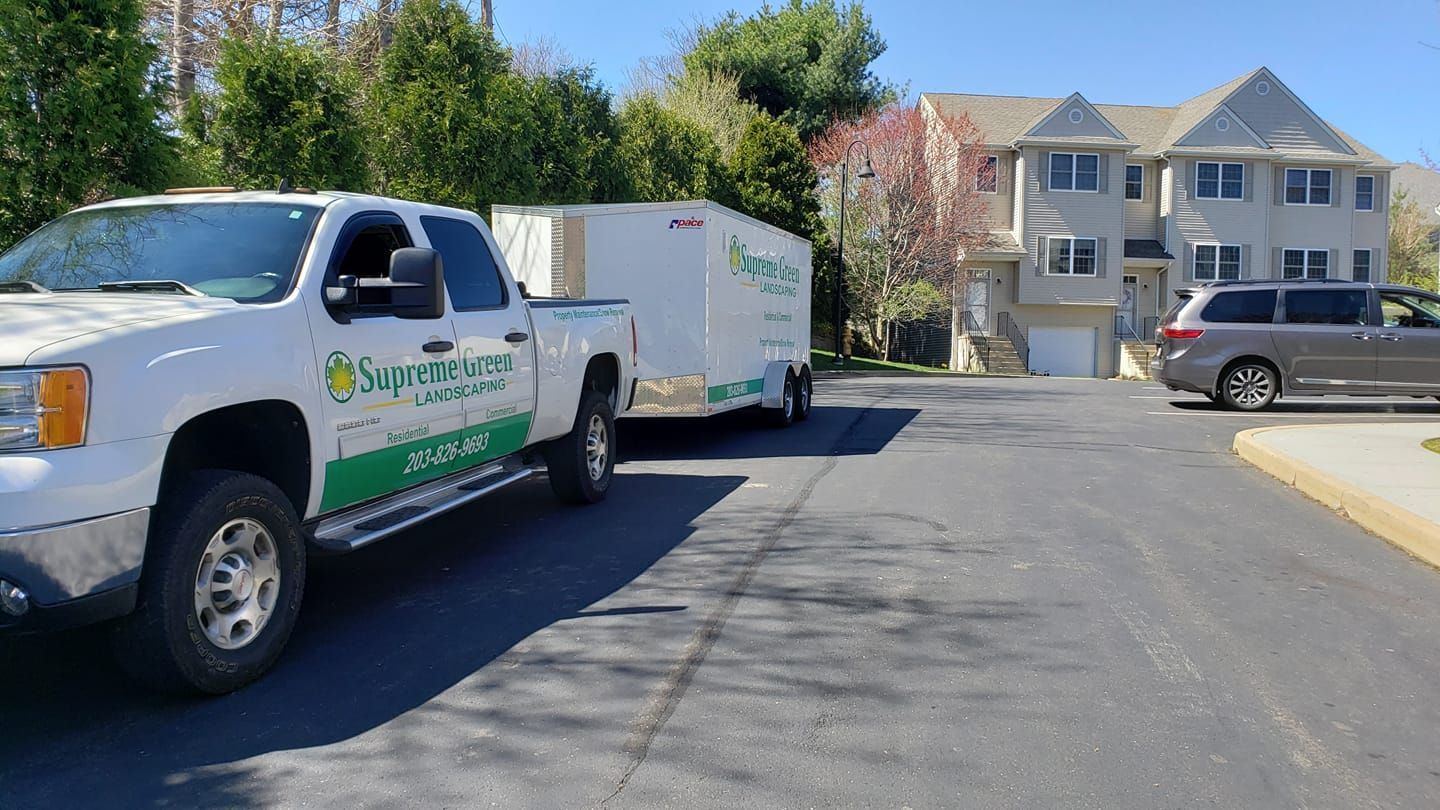 A white truck with a trailer attached to it is parked in front of a house.