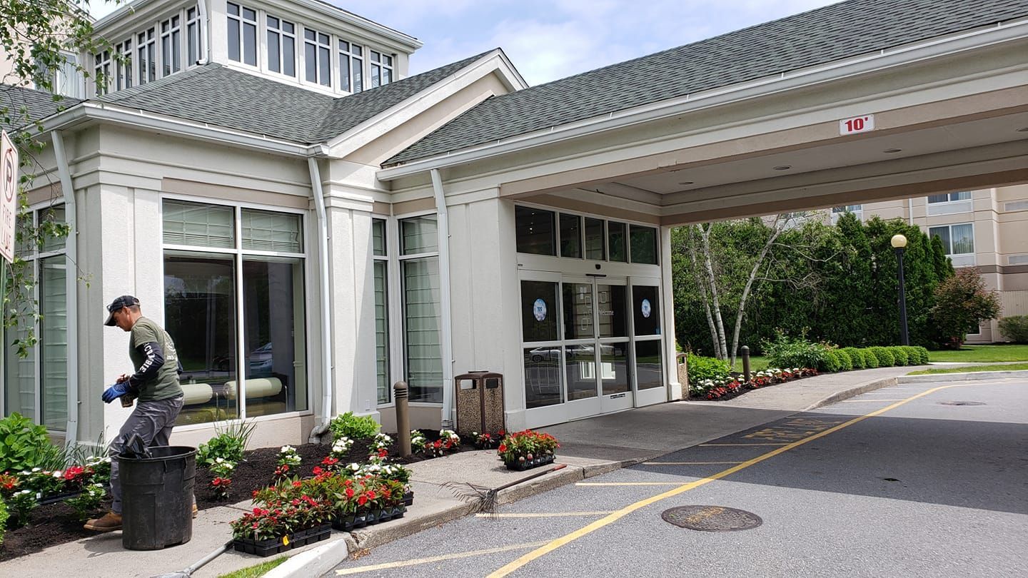 A man is watering flowers in front of a hotel.