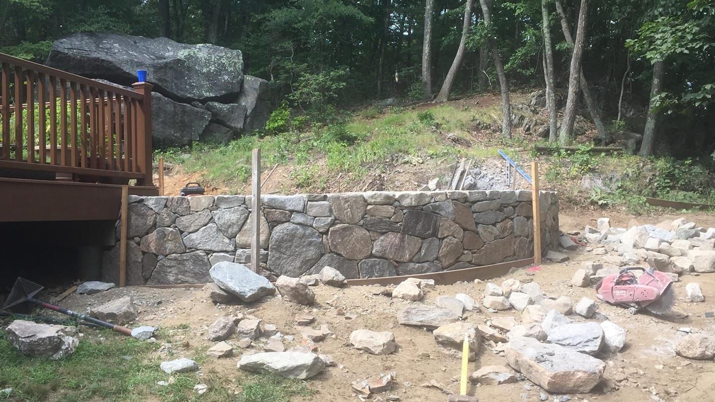 A stone wall is being built in a backyard next to a deck.