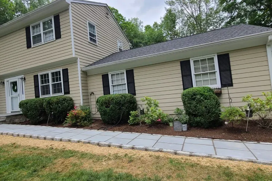 A beige house with black shutters and a walkway in front of it.