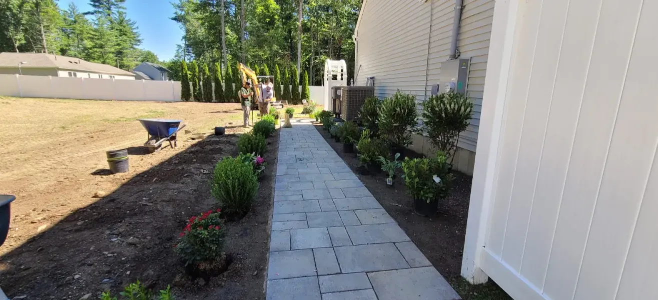 A walkway leading to a house with a white fence and a wheelbarrow.