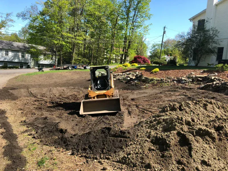 A bulldozer is moving dirt in a yard in front of a house.