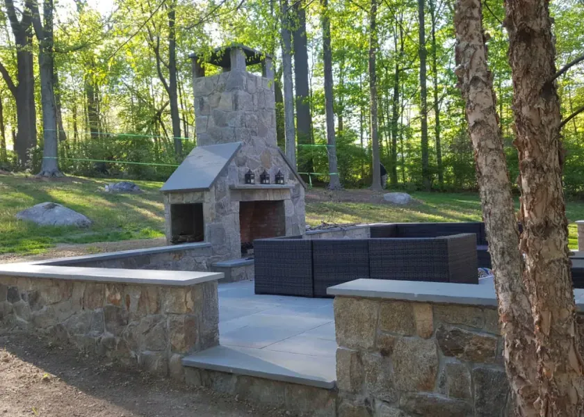 A patio with a fireplace and a couch in the woods
