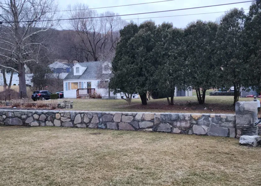 A stone wall surrounds a grassy field in front of a house.