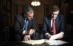 Two men in suits and ties are sitting at a table looking at papers.