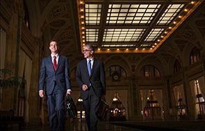 Two men in suits and ties are walking down a hallway.