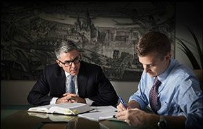 Two men are sitting at a table looking at a book.