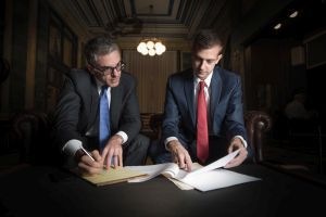 Two men in suits and ties are sitting at a table looking at papers.