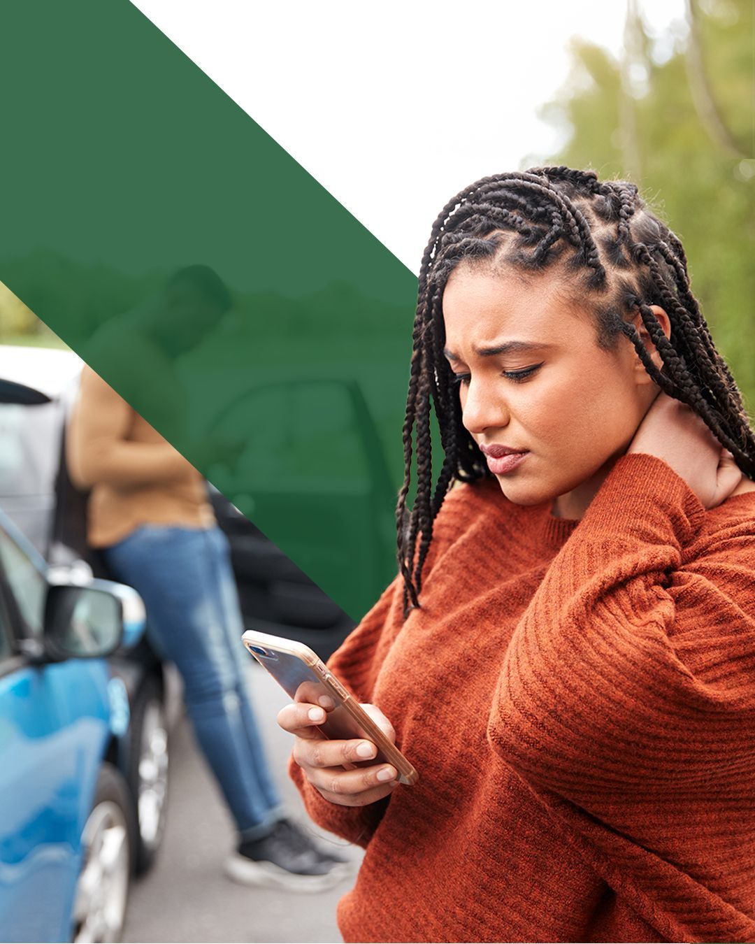 Woman holding her neck while checking her phone after a car accident, with damaged vehicles