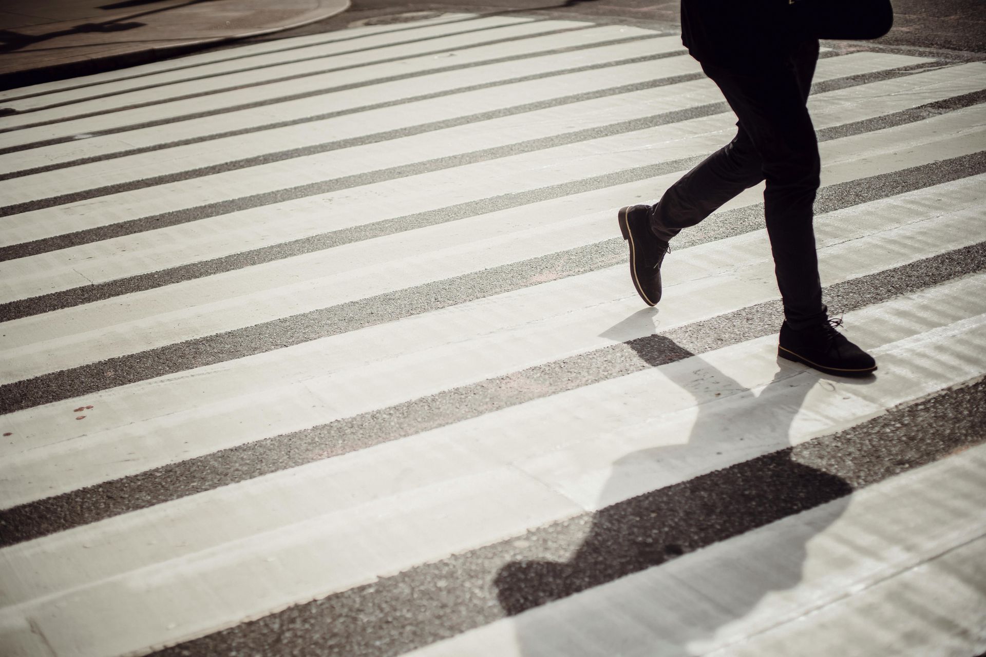 A person is crossing a crosswalk with their shadow on the ground.