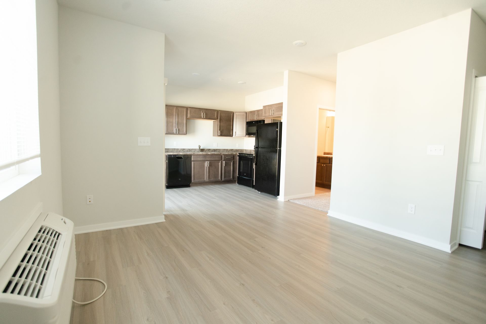 An empty living room with hardwood floors and a refrigerator.