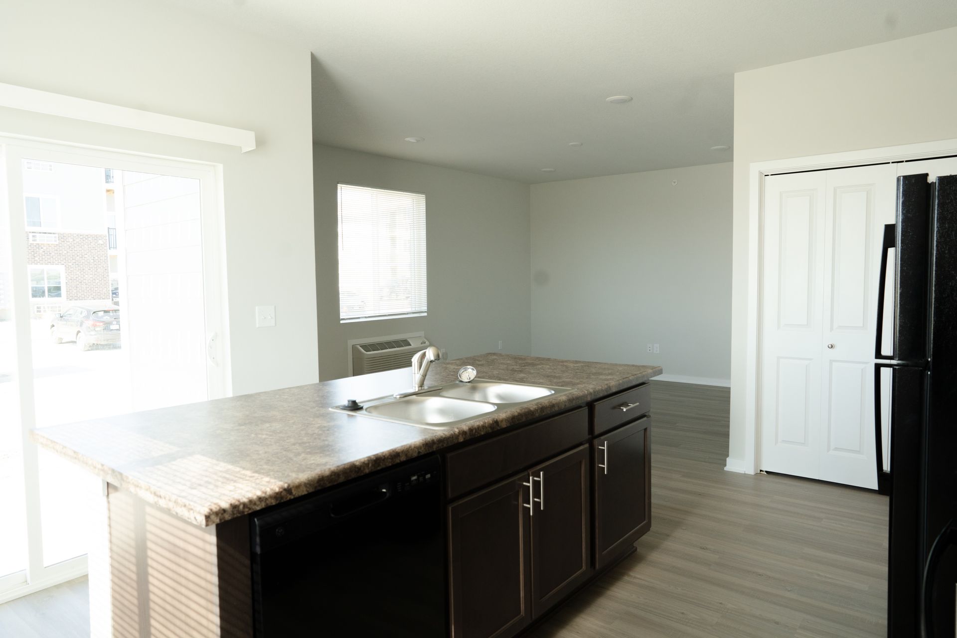An empty kitchen with a black refrigerator , sink , and dishwasher.