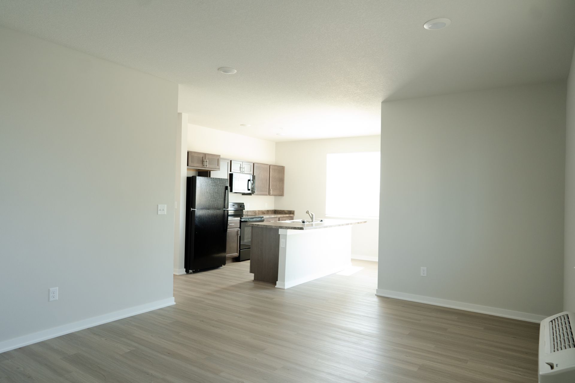 An empty living room with a kitchen in the background.