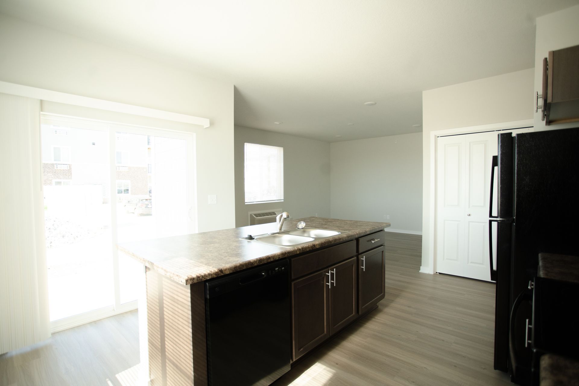 An empty kitchen with a black refrigerator , sink , and dishwasher.
