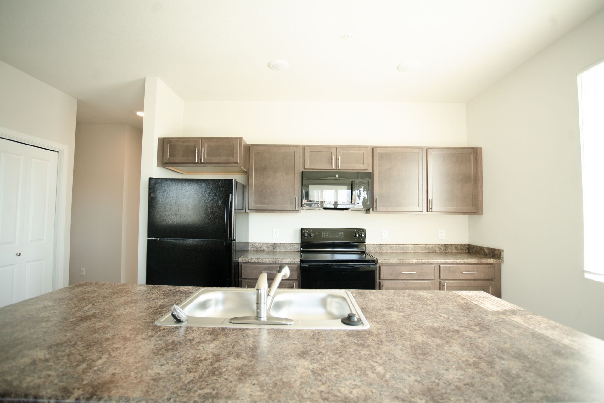 An empty kitchen with a sink , stove , refrigerator and microwave.