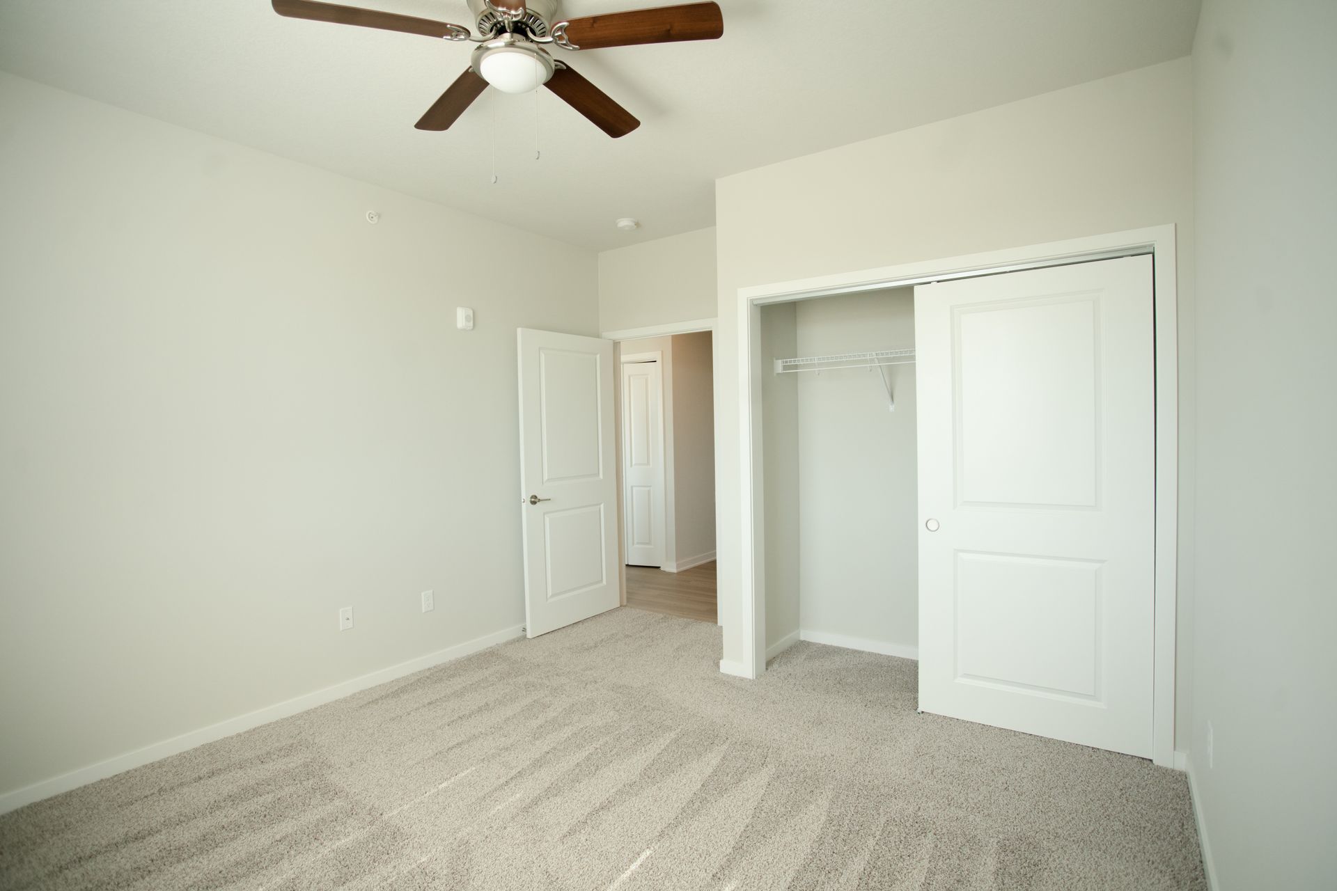An empty bedroom with a ceiling fan and a closet.