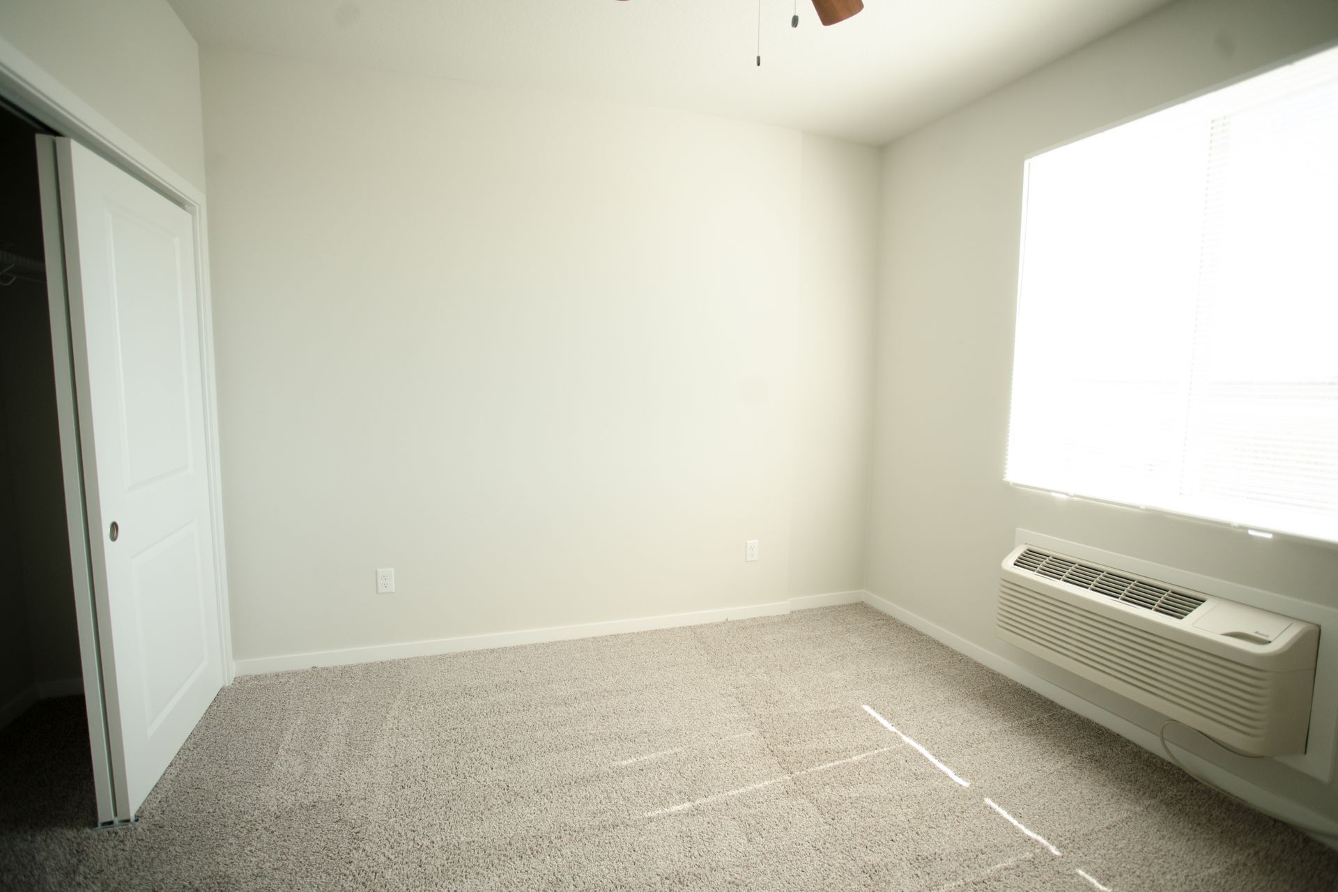 An empty bedroom with a window and a ceiling fan.