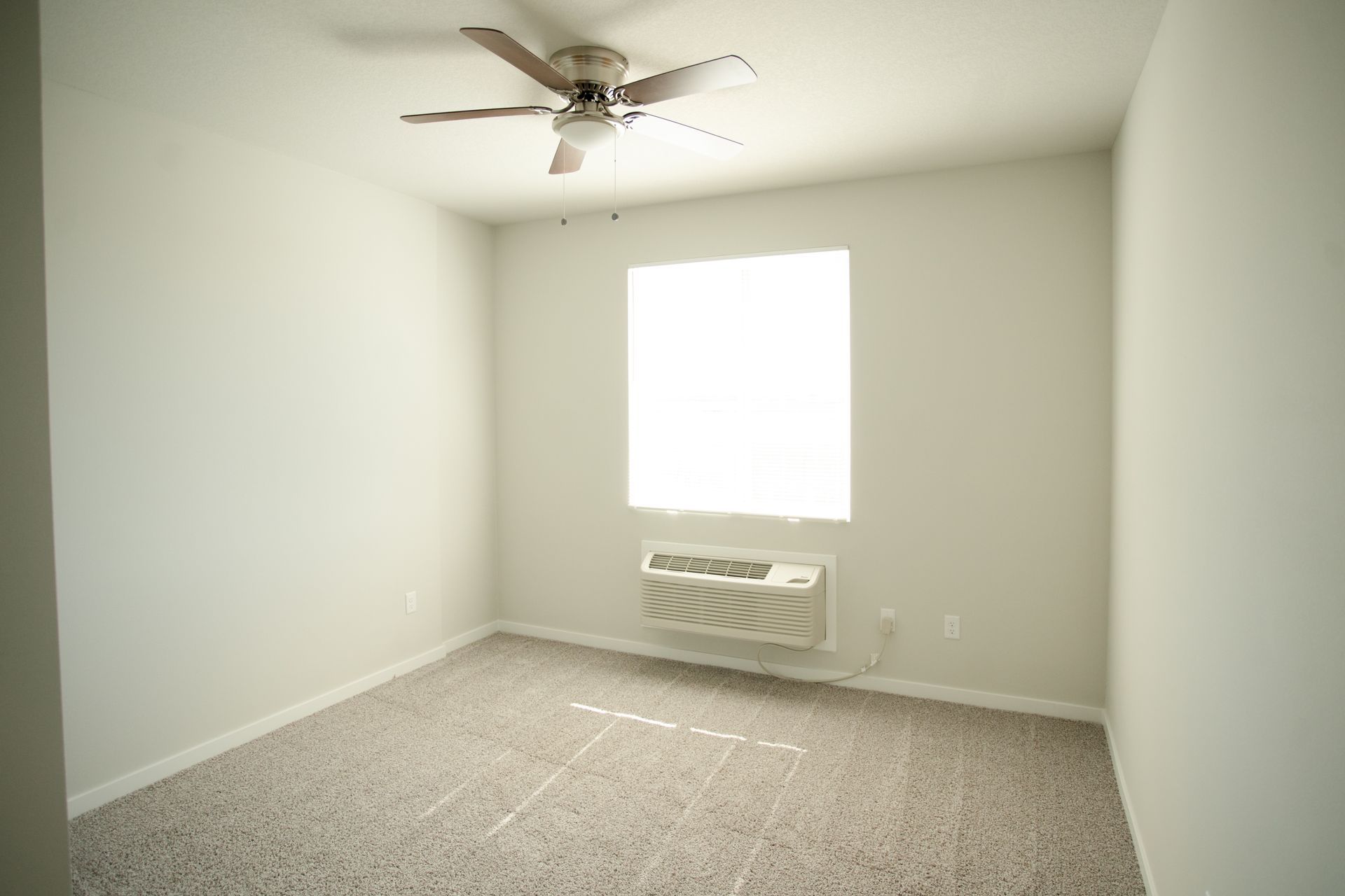 An empty bedroom with a ceiling fan and a window.
