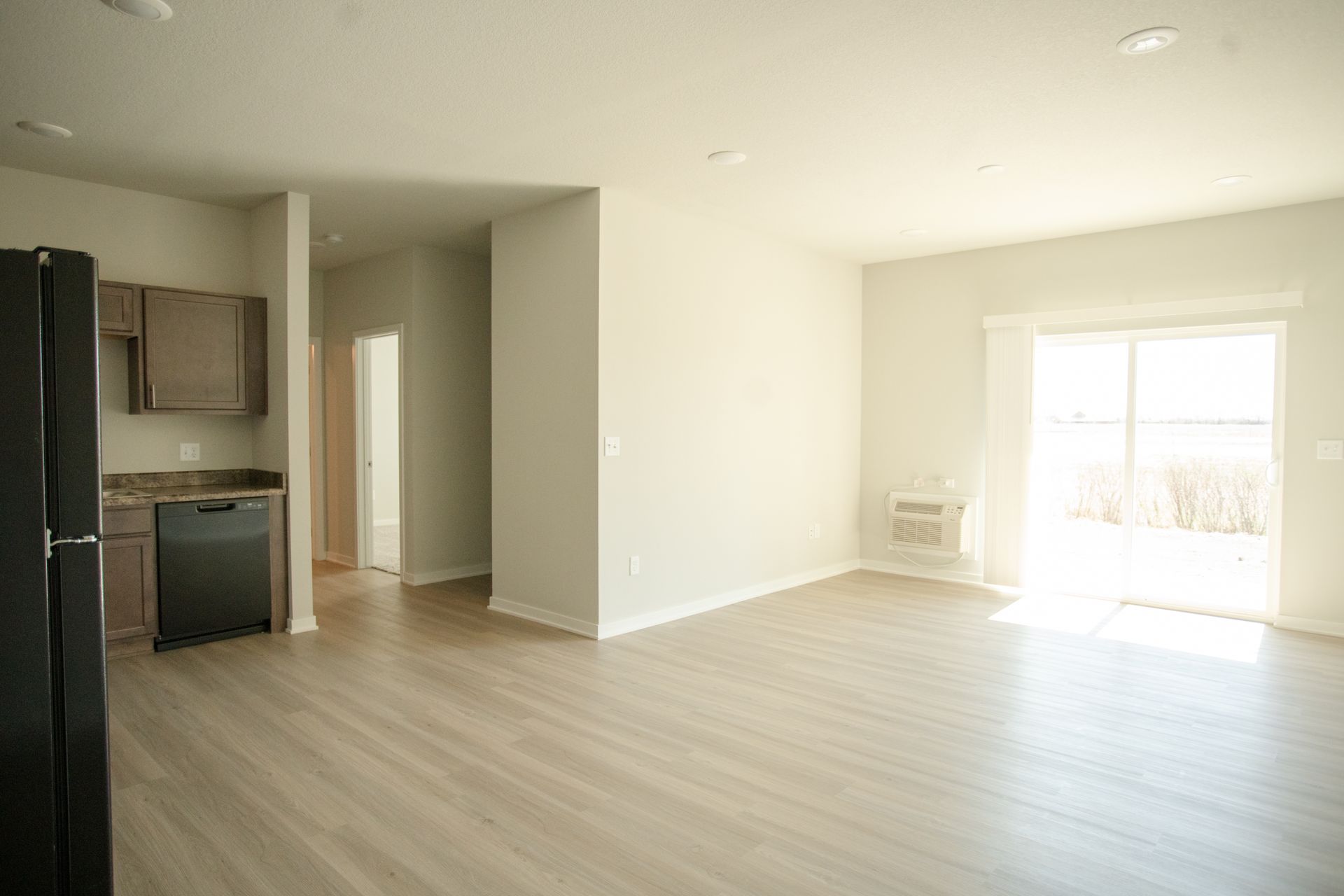 An empty apartment with a kitchen , living room , and sliding glass doors.