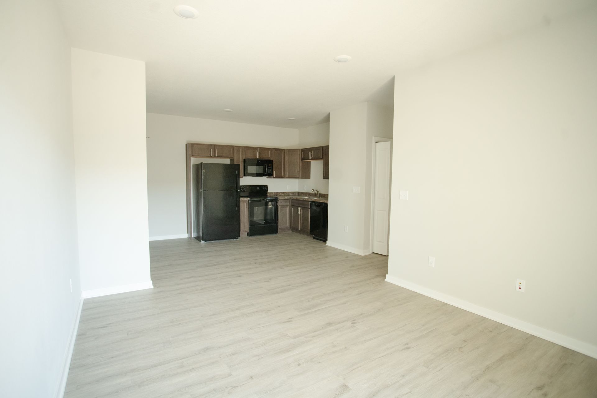 An empty living room with a kitchen in the background.
