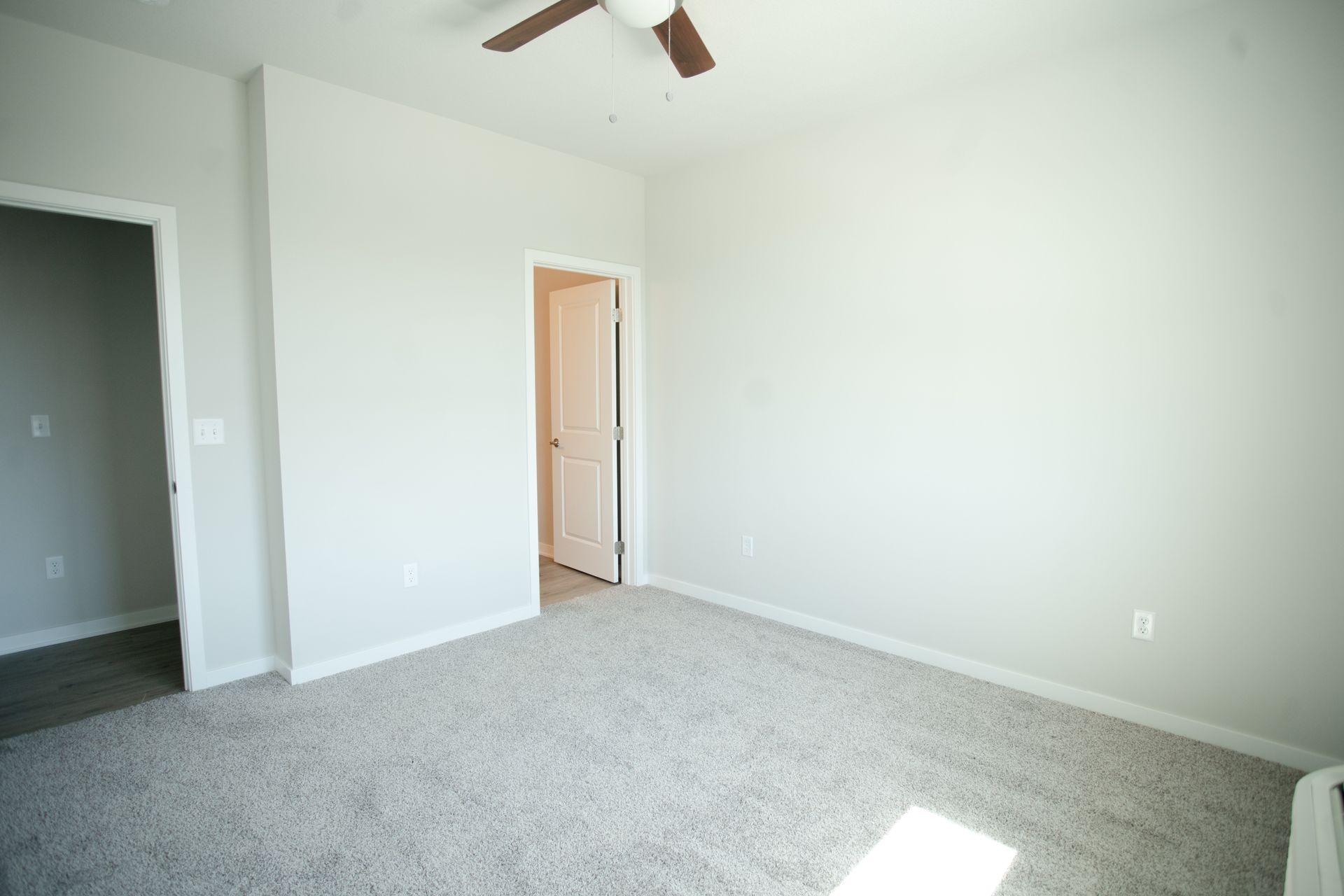 An empty bedroom with a ceiling fan and a door.
