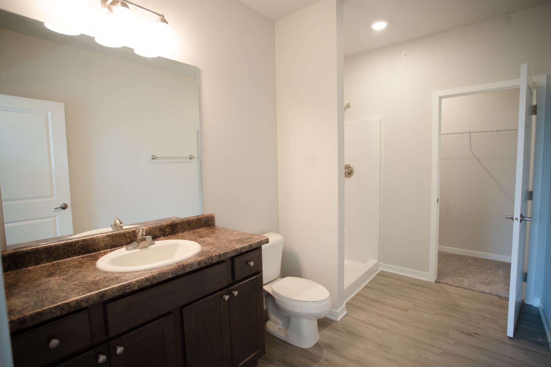 A bathroom with a sink , toilet , mirror and walk in shower.