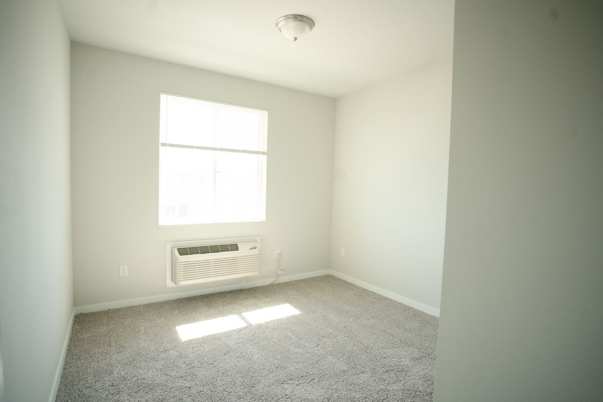 An empty bedroom with a window and air conditioner.