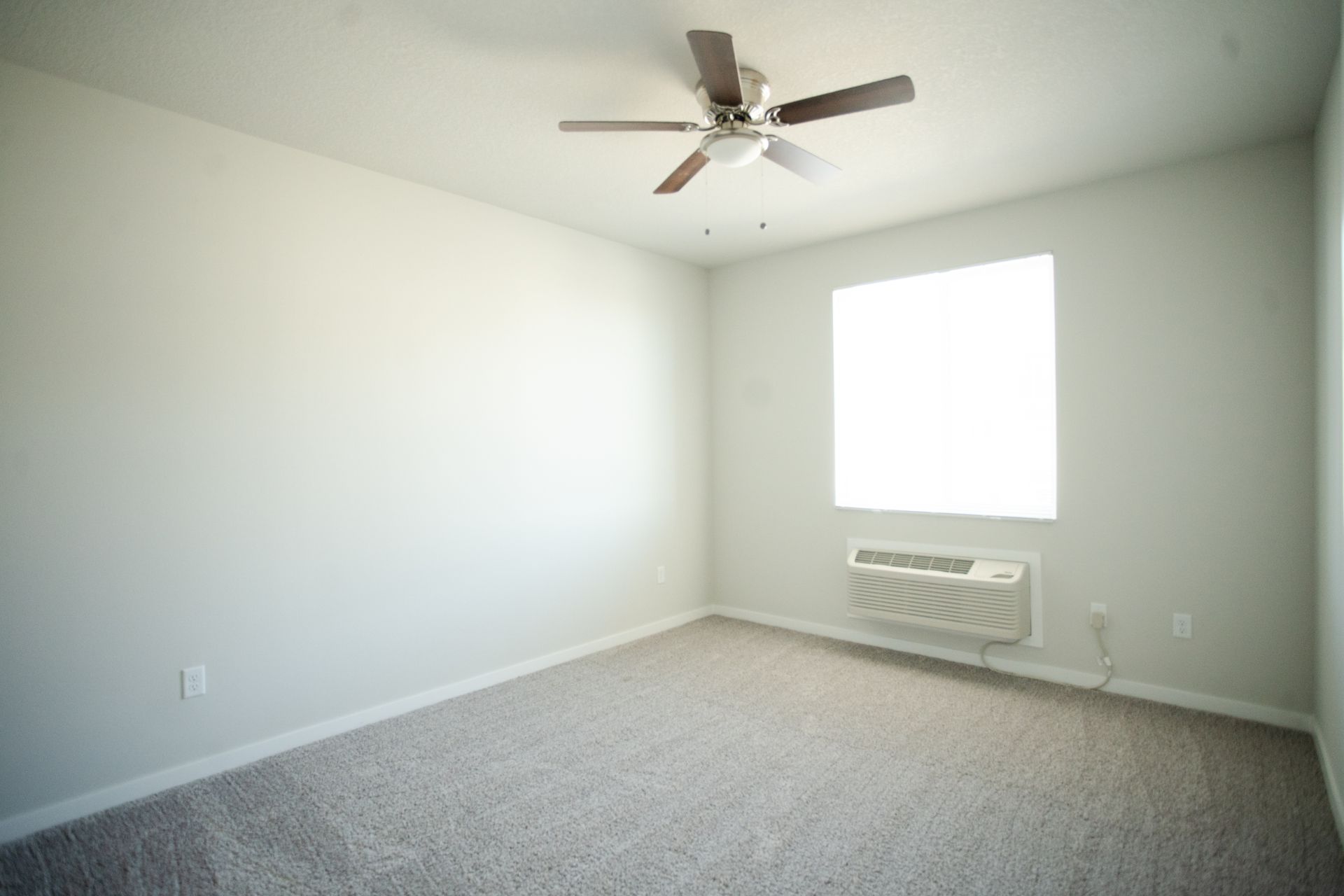 An empty bedroom with a ceiling fan and a window.