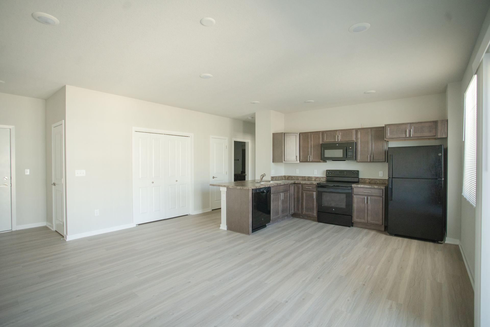An empty kitchen with a black refrigerator , stove , microwave and sink.