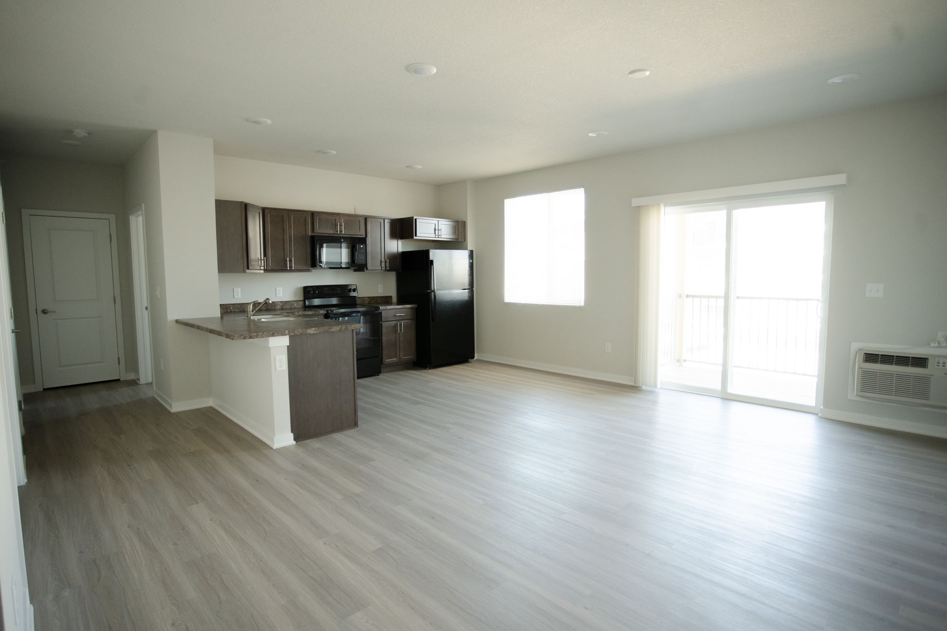 An empty apartment with a kitchen and sliding glass doors.