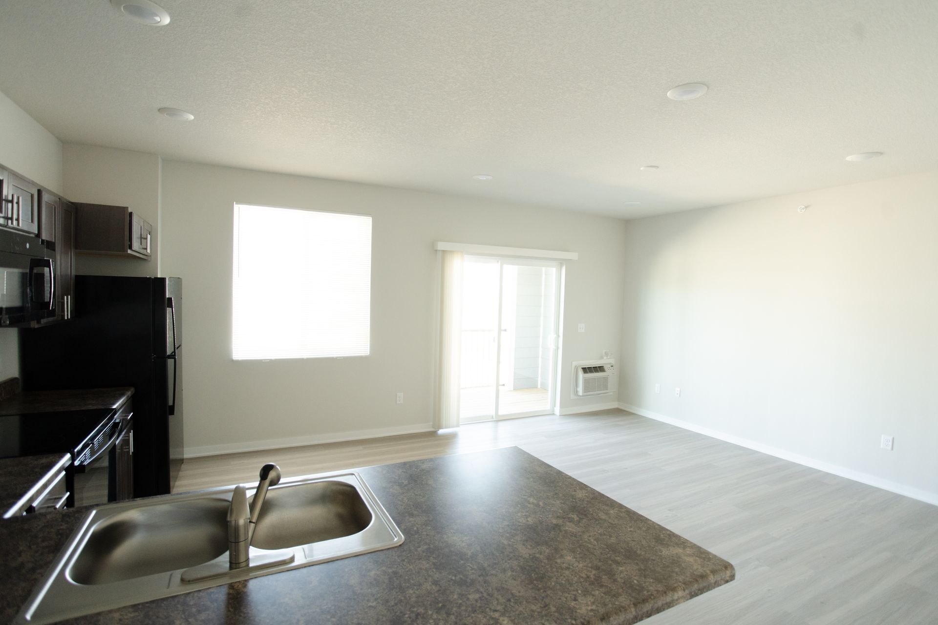 A kitchen with a sink , refrigerator , microwave and sliding glass doors.