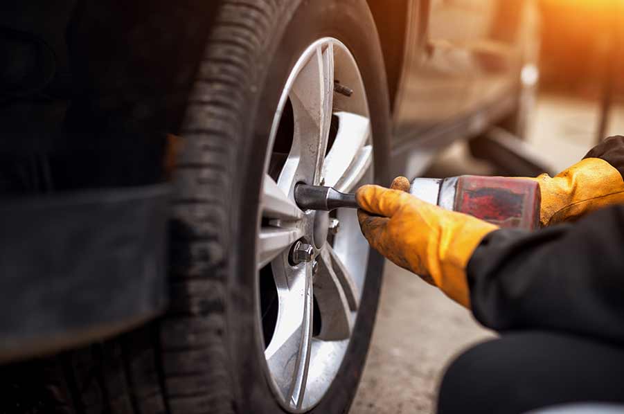A man is changing a tire on a car with a wrench.