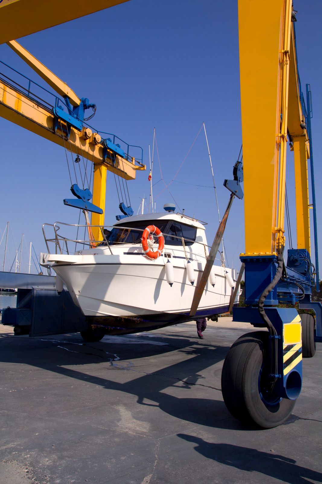 Boat being lifted by a large yellow crane on a sunny day.