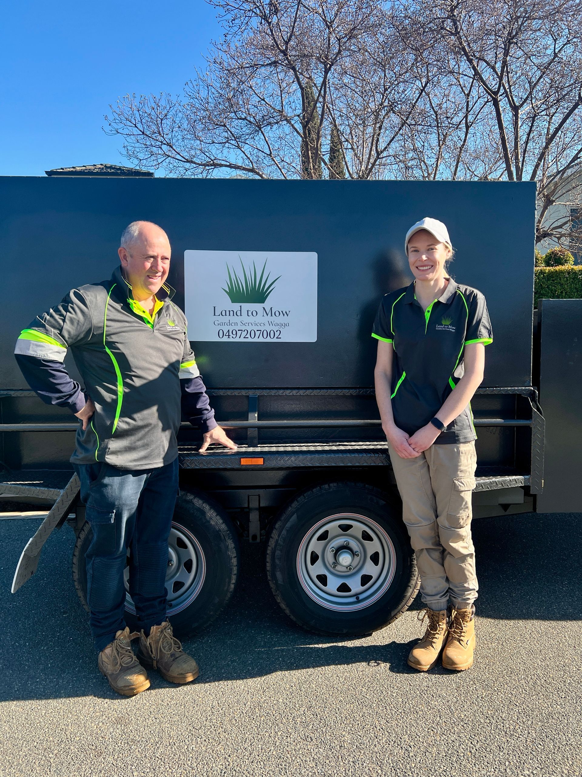 A Man and Woman Stand In Front Of Black Ute With Logo — Land to Mow Garden Services Wagga In Junee, NSW