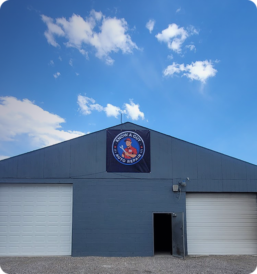 A blue auto repair shop with a banner, two garage doors, and an open entrance, under a bright blue sky with clouds | Know A Guy Auto Repair