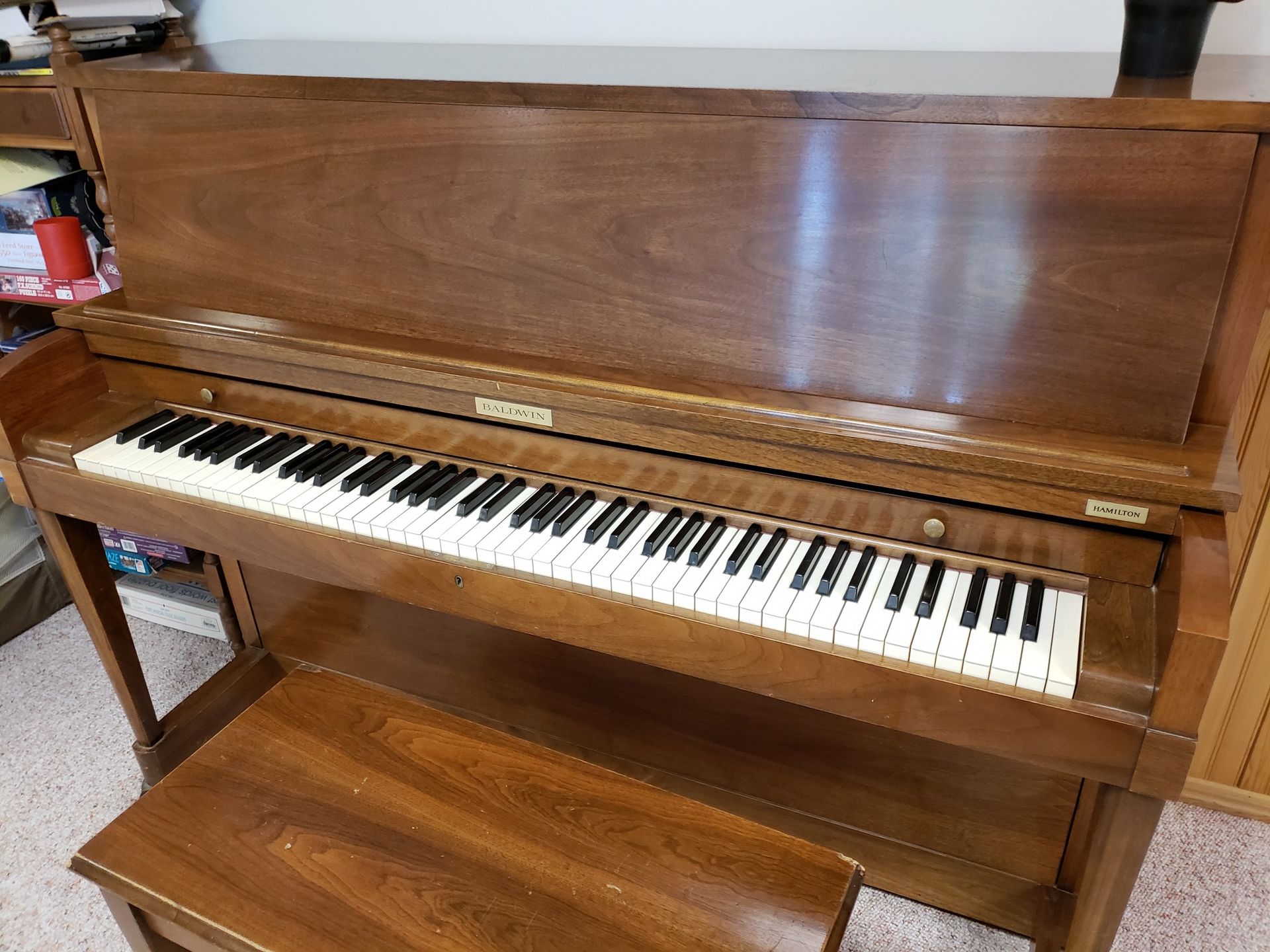 Wooden upright piano with bench; keys visible, in a room.