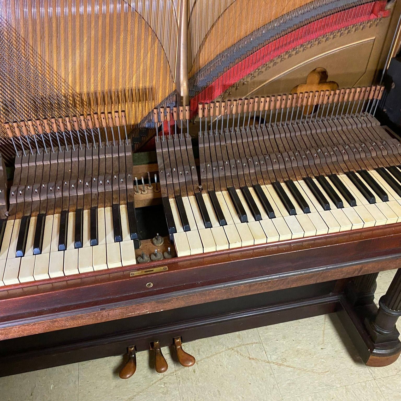 Close-up of a disassembled antique piano with ivory keys, strings, and wooden pedals.