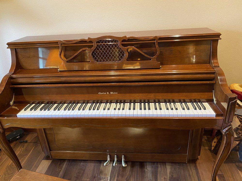 Upright brown piano with white and black keys, ornate wood design, three pedals.