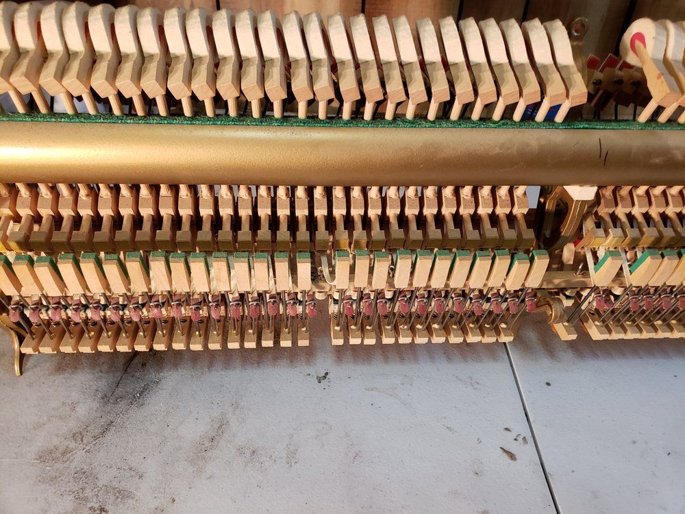 Piano keys and hammers, wooden mechanism, gold-colored beams, various levers and springs.