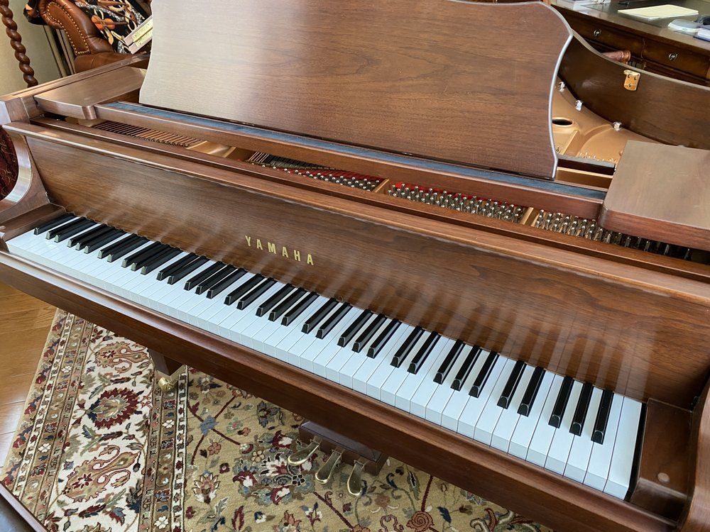 Brown Yamaha grand piano with open lid, keys visible, sitting in a room on a patterned rug.