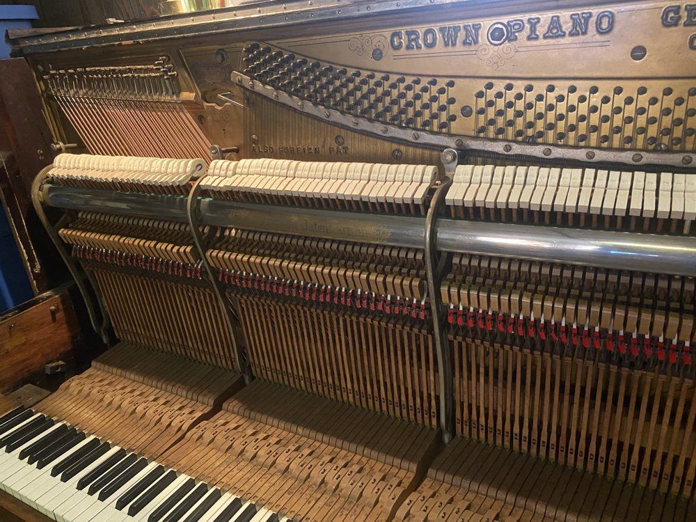 Interior of a Crown piano, showing hammers, strings, and keys. Gold-toned with wood and black/white keys.