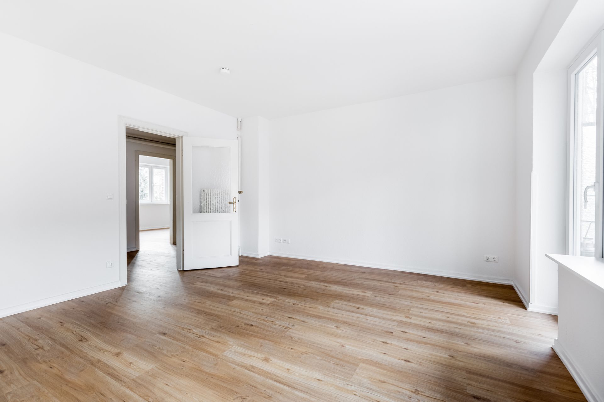 An empty living room with hardwood floors and white walls.
