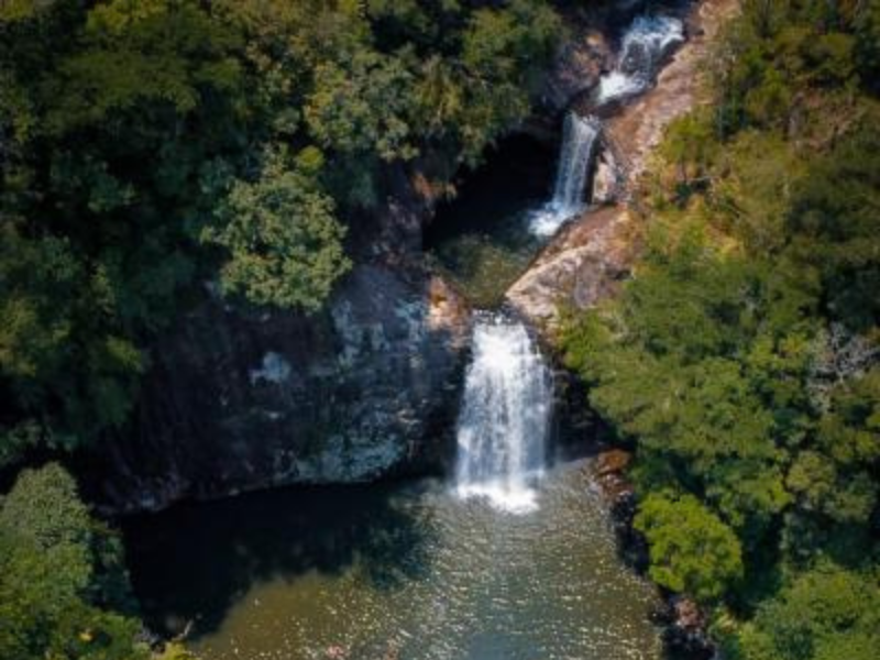 Duas cascatas despencam por uma encosta rochosa cercada por árvores verdejantes, criando uma piscina natural abaixo.