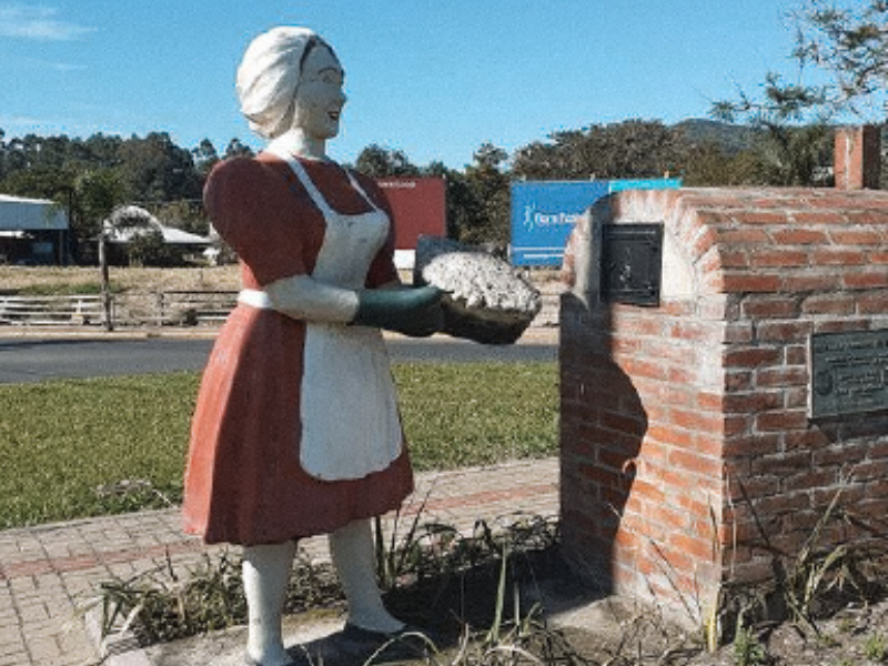 Estátua de uma mulher com vestido vermelho e avental branco segurando pão