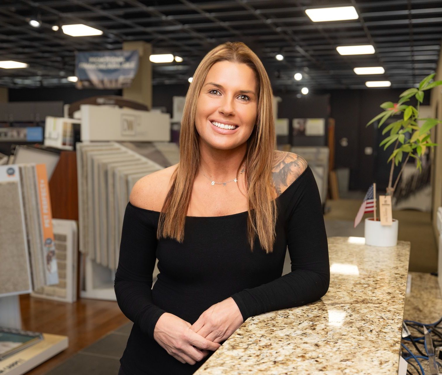 A woman in a black dress is leaning on a counter in a store.