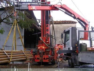 Piattaforma di perforazione rossa con gru che solleva i tubi. Camion parcheggiato di lato, all'aperto.