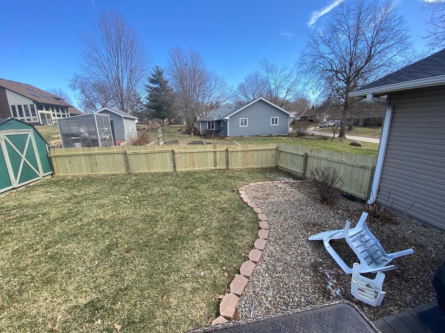 Backyard with a wooden fence, a shed, and a small garden bed. A white chair is fallen over on the right side.