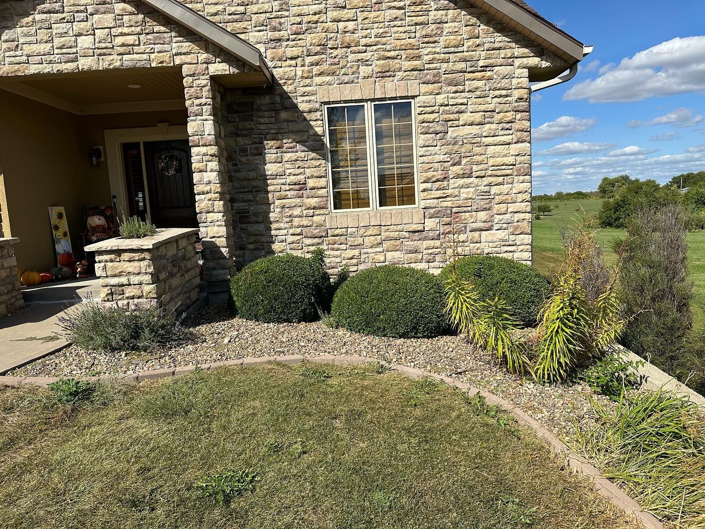 Stone house with front yard landscaping, including bushes and grass, under a blue sky.