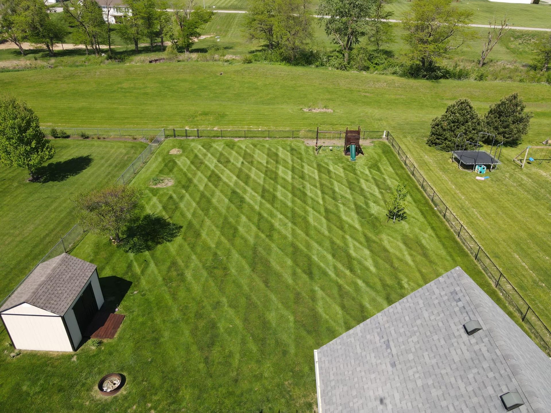 Aerial view of a lawn with a patterned mowing design. A shed and home with a grey roof are in the shot.