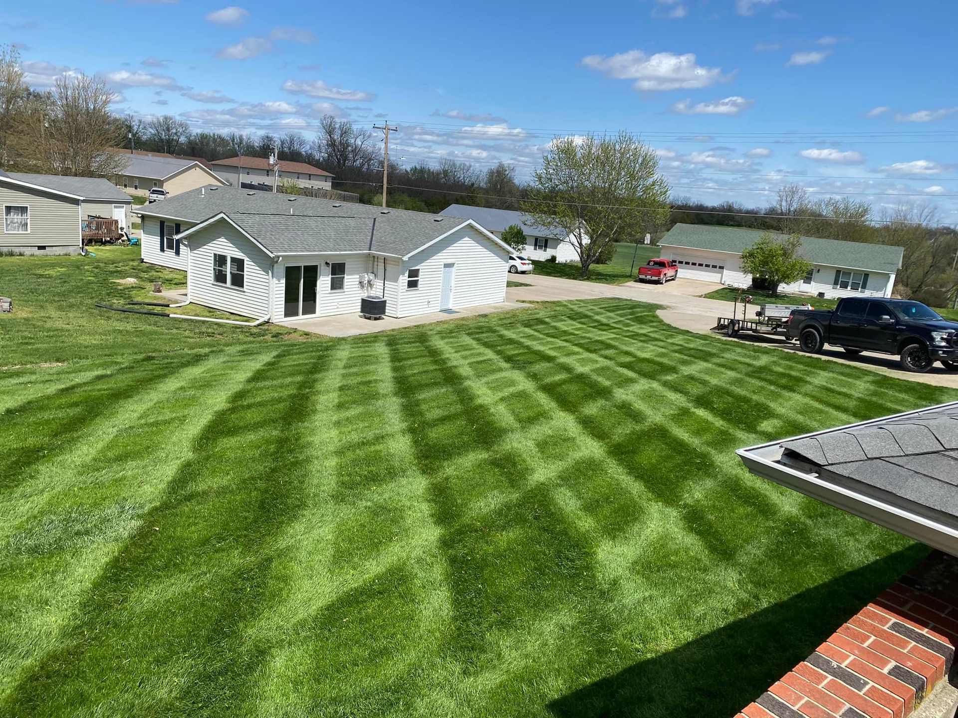 Brick pathway leading to a red and brown house with a porch. Landscaping, grass, and gravel border the pathway.